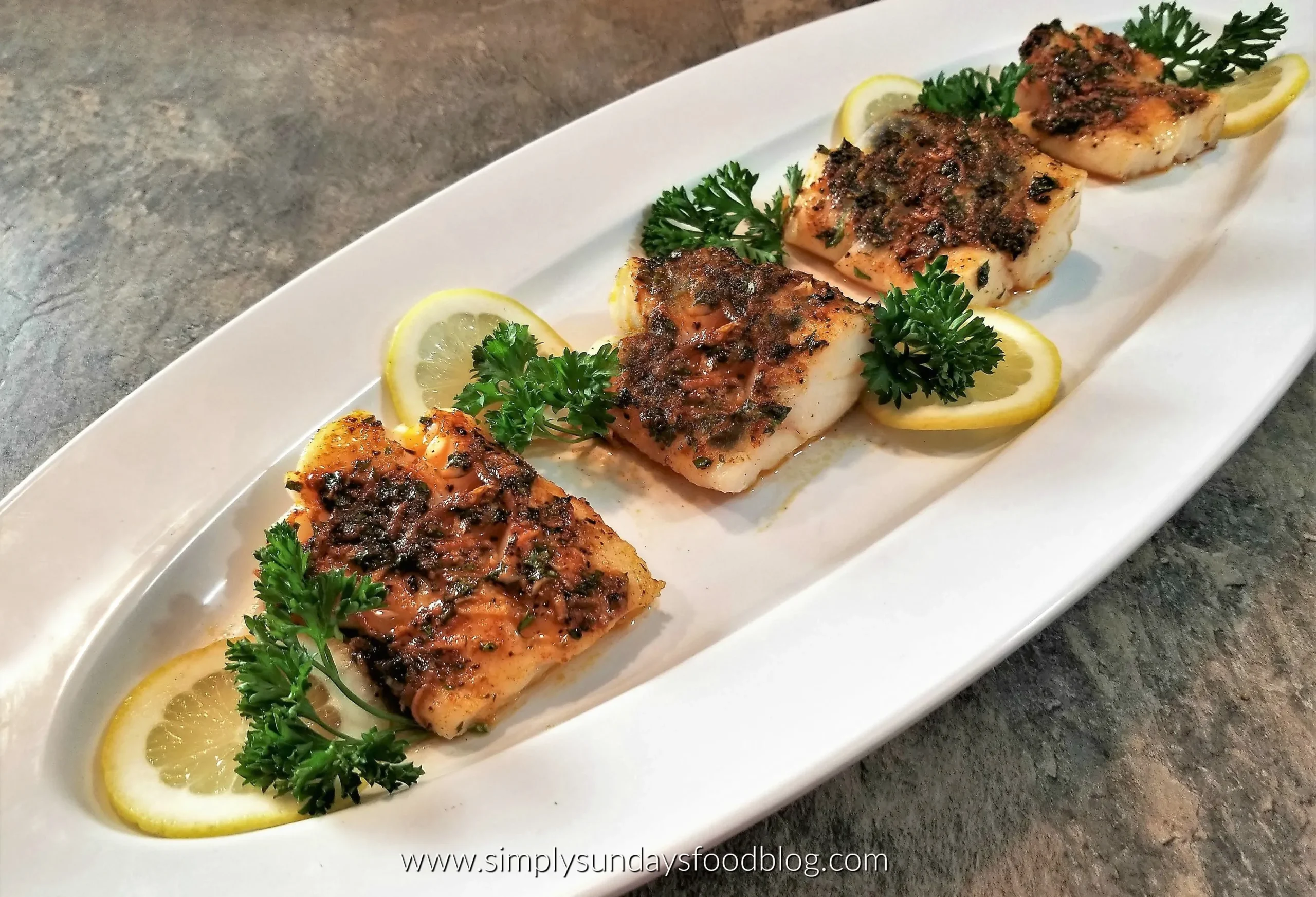 Plated broiled cod garnished with dill and lemon alongside roasted asparagus and quinoa.