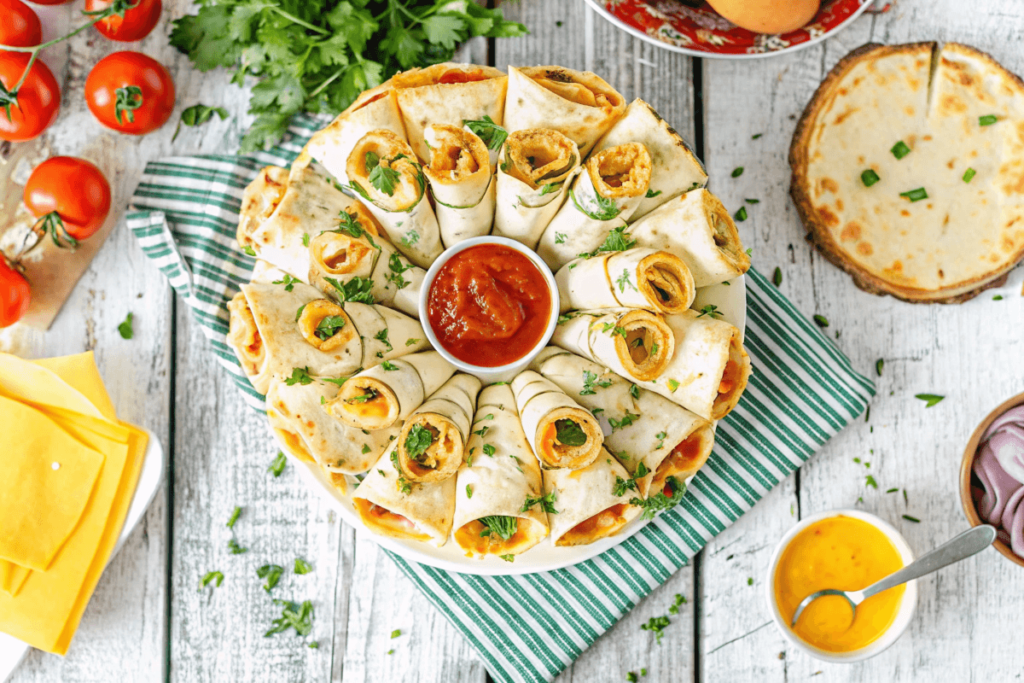 A baked blooming quesadilla ring on a serving platter surrounded by dips, with happy guests grabbing pieces.