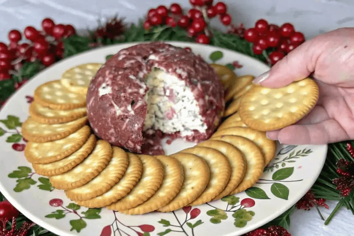 A finished dried beef cheese ball on a serving platter, garnished with green onions and surrounded by an assortment of crackers.